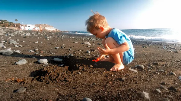 Mały chłopczyk bawiący się na plaży z plastikową łopatą i budującym zamek z piasku — Zdjęcie stockowe
