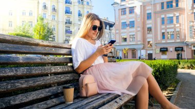 Güzel seksi kadın bankta oturuyor ve akıllı telefon kullanıyor.