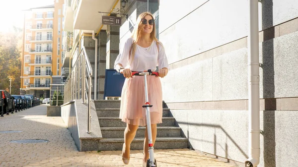 Beautiful young woman in skirt riding on scooter at early morning — Stock Photo, Image