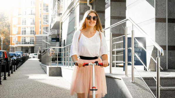 Felice sorridente ragazza cavalcando su scooter calcio sulla stretta strada della città — Foto Stock