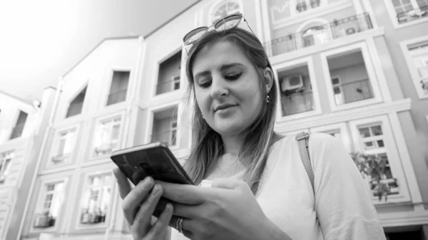 Zwart-wit portret van jonge vrouwelijke student met smartphone op straat — Stockfoto