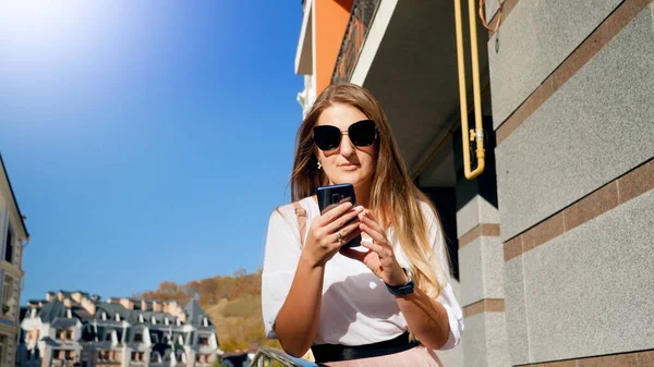 Portrait de belle jeune femme en lunettes de soleil tapant message sur smartphone — Photo