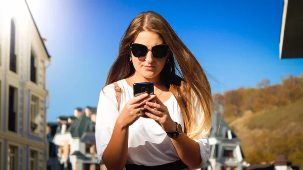 Retrato de jovem mulher concentrada digitando mensagem no smartphone na rua da cidade — Fotografia de Stock
