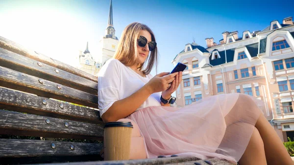 Portrét krásné ženy s dlouhými vlasy sedí na lavičce a psaní zprávy na mobilním telefonu — Stock fotografie