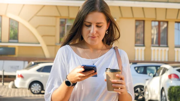 Retrato de bela trabalhadora andando na rua da cidade com copo de café e smartphone de navegação — Fotografia de Stock