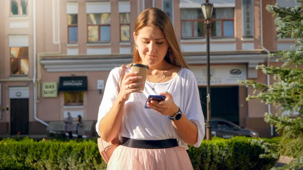 Bella giovane donna in possesso di tazza di carta da caffè in una mano e smartphone in altra mano — Foto Stock