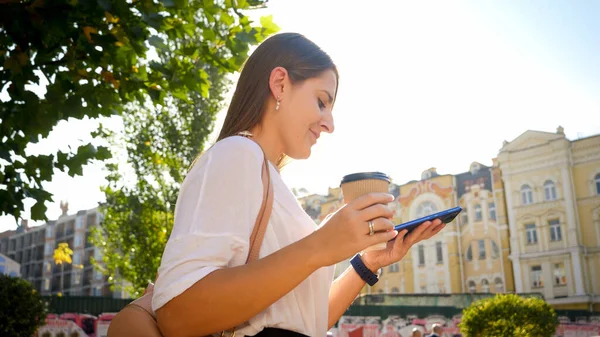 Porträt einer schönen Studentin, die mit Kaffee und Smartphone im Park spaziert — Stockfoto