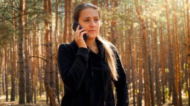 Ormanda yürürken telefonla konuşan genç bir kadın yürüyüşçünün portresi.