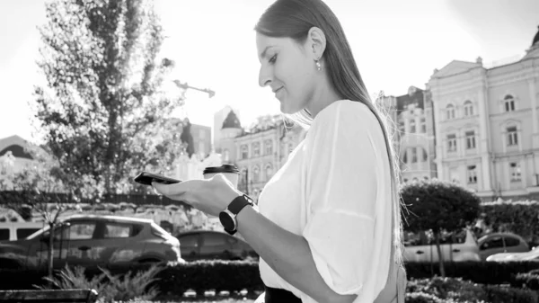 Черно-белый портрет занятой молодой женщины, идущей по городу и печатающей сообщения на смартфоне — стоковое фото