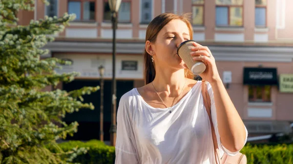 Портрет красивой стильной девушки, пьющей кофе из бумажной чашки во время прогулки по городской улице — стоковое фото