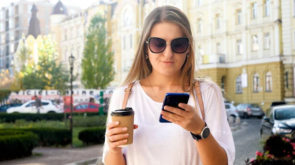 Portrait of beautiful female student with cup of coffee browsing internet on smartphone — Stock Photo, Image