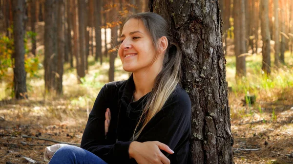 Närbild porträtt av glad leende flicka sitter i skogen och lutar sig mot tall. Begreppet frihet och harmoni med naturen. — Stockfoto