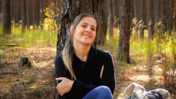 Retrato de una hermosa mujer sonriente apoyada en el pino en el bosque después de largas caminatas y viajes — Foto de Stock