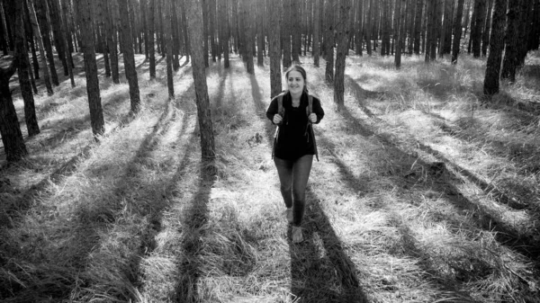 Black and white photo of smiling young woman with backpack hiking in the forest — Stock Photo, Image