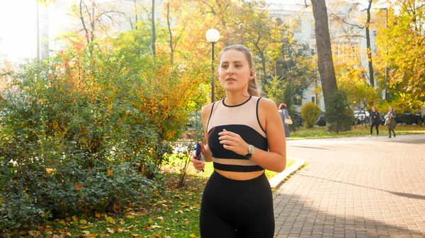 Portrait of beatiful young woman listening to music and running at autumn park — Stock Photo, Image