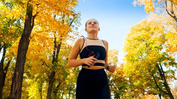 Portrait of beautiful smiling woman with earphones running at atumn park — Stock Photo, Image