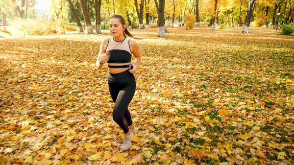 Sexy woman in sports outfit running on fallen tree leaves at autumn park — Stock Photo, Image