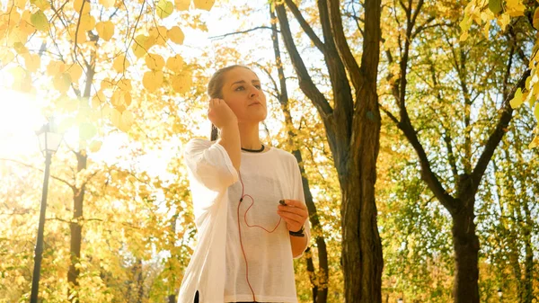 Portrait of beautiful young woman putting on headphones with music before jogging at autumn park — Stock Photo, Image