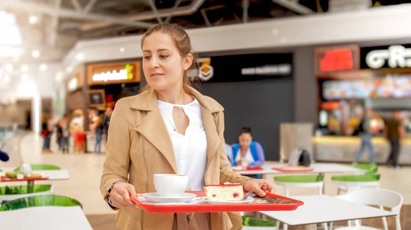 Retrato de una joven sosteniendo comida en bandeja buscando un lugar para comer en el patio de comidas en el centro comercial — Foto de Stock