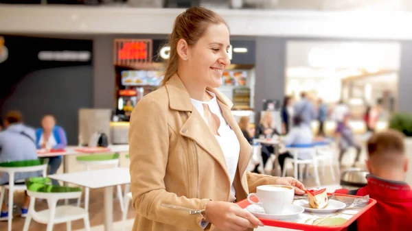 Potret wanita muda tersenyum berjalan di kafe dengan sarapan di atas nampan plastik — Stok Foto
