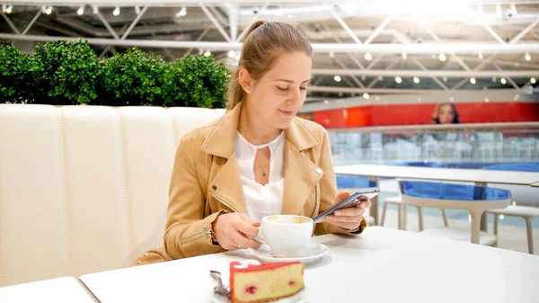 Porträt einer lächelnden jungen Frau, die morgens im Café sitzt und das Smartphone benutzt — Stockfoto