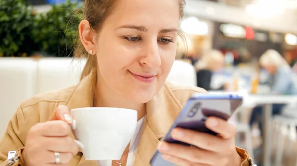 Portré fiatal nő iszik kávét és böngészés interneten okostelefon a kávézóban — Stock Fotó