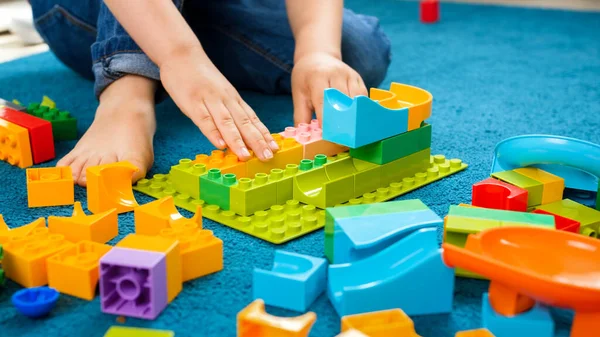 Närbild av lilla barn pojke sitter på mattan hemma och leka med färgglada konstruktör block — Stockfoto