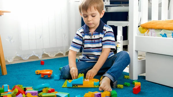 Portret małego chłopca siedzącego na podłodze w sypialni i bawiącego się z konstruktorem zabawek — Zdjęcie stockowe