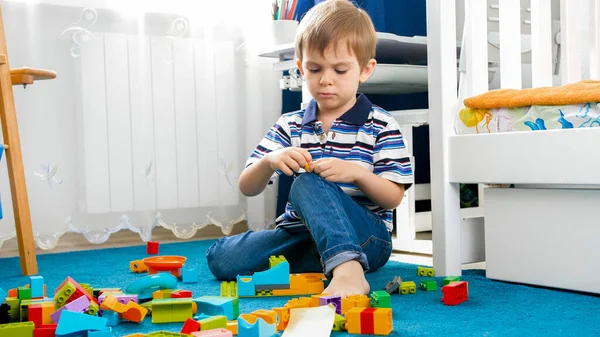 Portrait of little concentrated boy palying on carpet with toy blocks — Stock Photo, Image