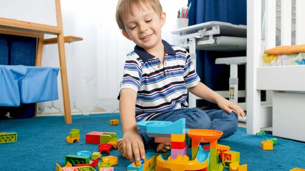 Portret uśmiechniętego chłopca bawiącego się kolorowymi klockami konstrukcyjnymi na dywanie w pokoju zabaw — Zdjęcie stockowe