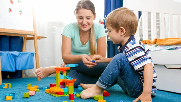 Portret van vrolijke lachende jongen met jonge moeder spelen op de vloer met kleurrijk speelgoed — Stockfoto