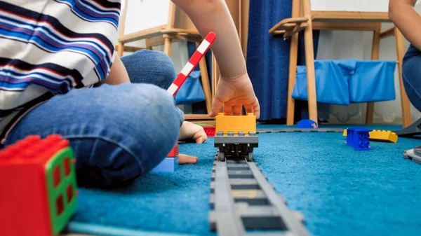 Mały 4-letni chłopiec siedzi na dywanie i bawi się zabawkowymi pociągami — Zdjęcie stockowe