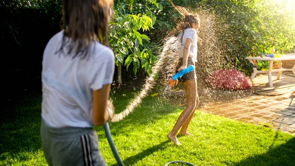 Dwie nastolatki bawią się w wodną walkę i pluskają wodą z węża ogrodowego — Zdjęcie stockowe