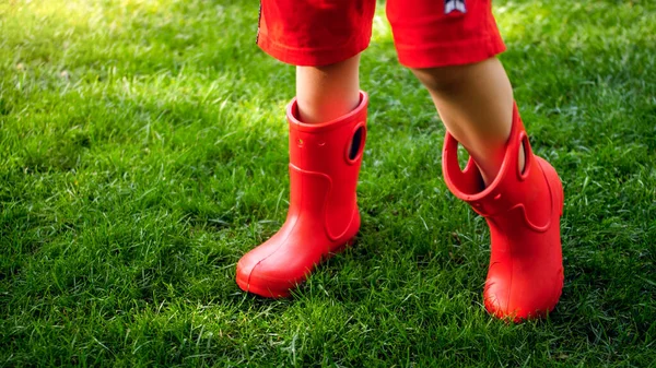 Closeup photo of childs feet in red rubber booy on fresh green grass — Stock Photo, Image