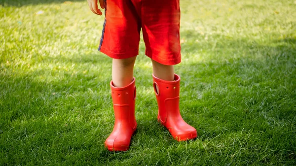 Foto de primer plano del niño con botas de goma rojas de pie sobre la hierba en el parque —  Fotos de Stock