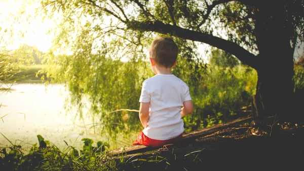 Foto tonica vista posteriore di bambino che pesca sul fiume al tramonto — Foto Stock