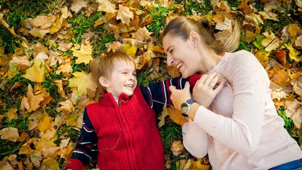 Porträtt av glad skrattande pojke med mamma liggande på höstlöv och kittlande varandra — Stockfoto