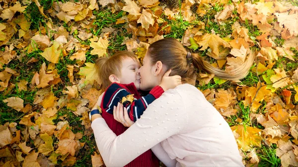 Portrait of little boy kissing his young mother lying on ground at autumn park — Stock Photo, Image