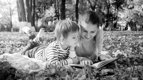 Black and white portrait of family reading story book while lying on ground at park — Stock Photo, Image