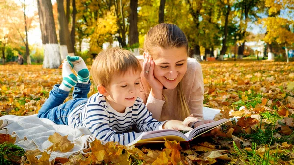 Portret van vrolijke lachende jongen met moeder leesboek op picknick in het herfstpark — Stockfoto