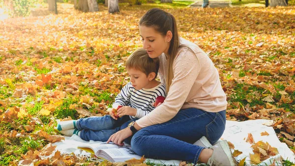 Ritratto tonico di giovane donna che legge un libro al suo piccolo figlio in picnic al parco autunnale — Foto Stock