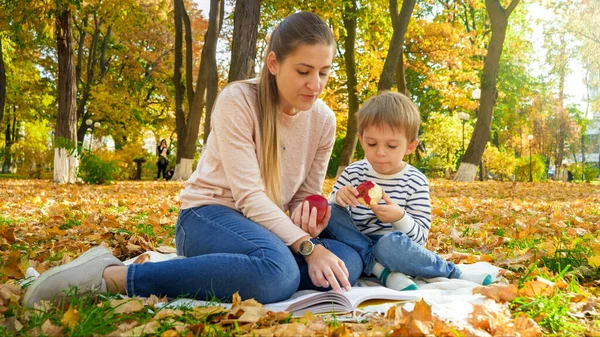 Счастливая семья, устраивающая пикник на одеяле в осеннем парке и читающая книгу — стоковое фото