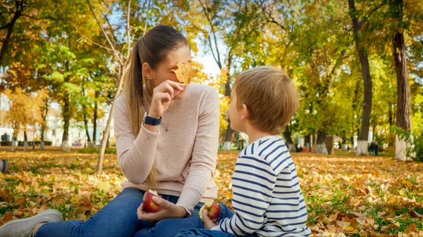 Mulher bonita olhando através da folha amarela do outono em seu filho no parque do outono — Fotografia de Stock