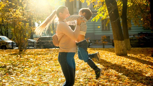 Piękne szczęśliwy matka przytula i przędzenia jej śmiejący się mały syn w jesiennym parku — Zdjęcie stockowe