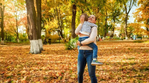 Gyönyörű mosolygós fiatal anya öleli kisfiát az őszi parkban — Stock Fotó