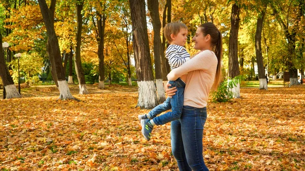 Retrato de la feliz y sonriente madre joven abrazando a su pequeño hijo en el parque de otoño — Foto de Stock