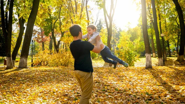 Giovane padre che tiene in braccio e gira il suo piccolo figlio nel parco autunnale — Foto Stock