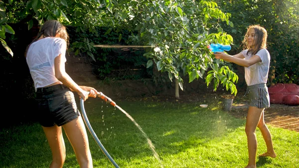 Två glada skrattande flickor stänk vatten och leka med vattenpistoler — Stockfoto