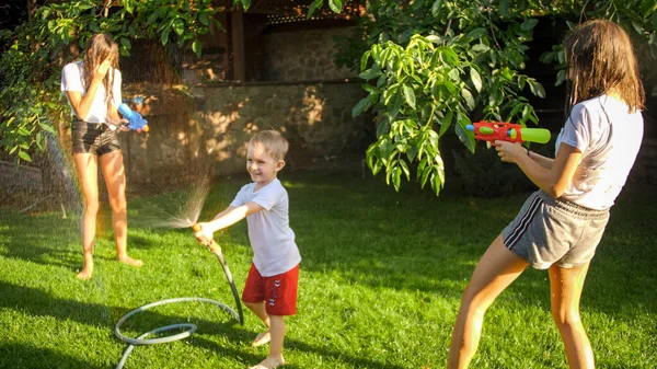 Glada skrattande barn leker med trädgårdsvattenslang i trädgården — Stockfoto