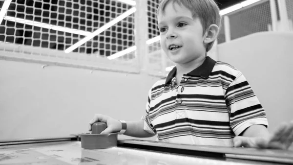 Svart och vitt porträtt av leende upphetsad pojke spelar air hockey i lekrummet i nöjesparken — Stockfoto